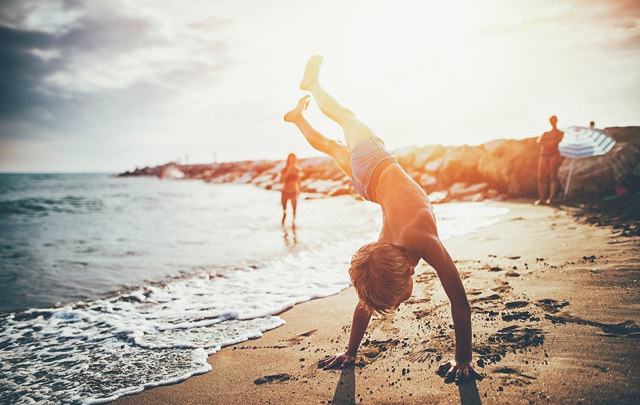 Little boy practicing handstand on beach
