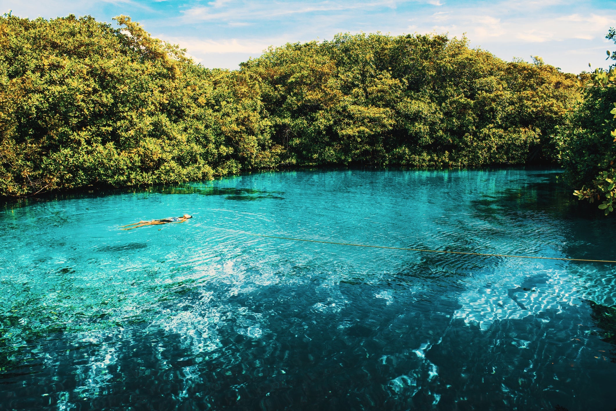 Woman floating in an open cenote in Tulum, Mexico