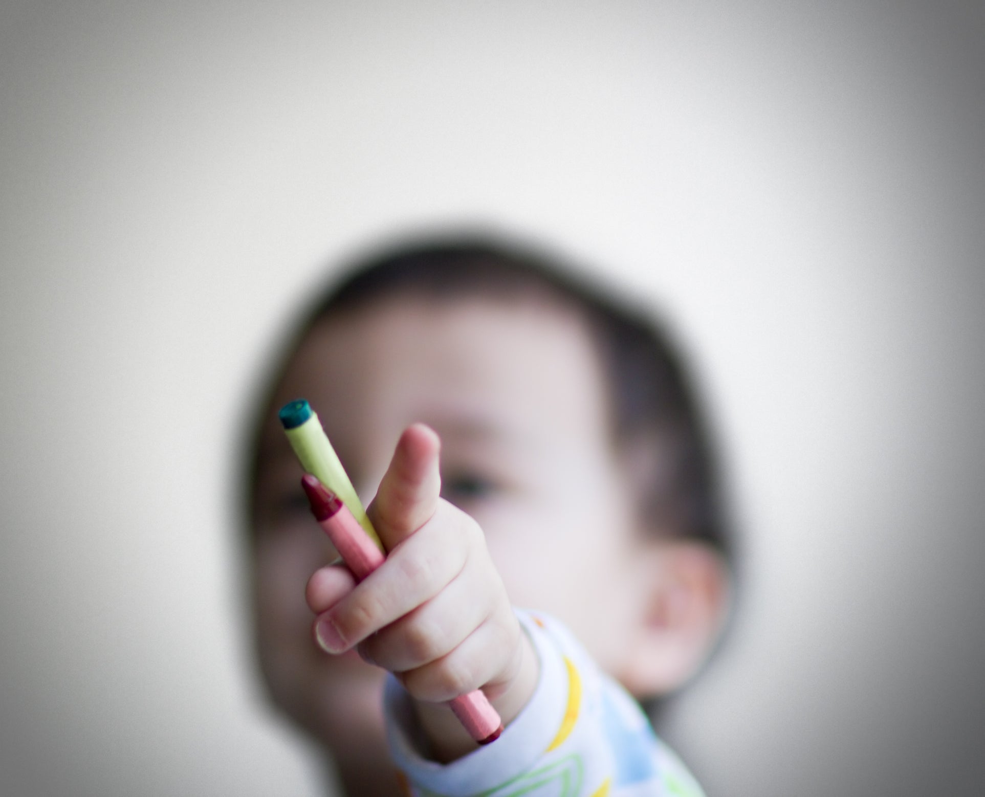 Toddler holding crayons and pointing index finger