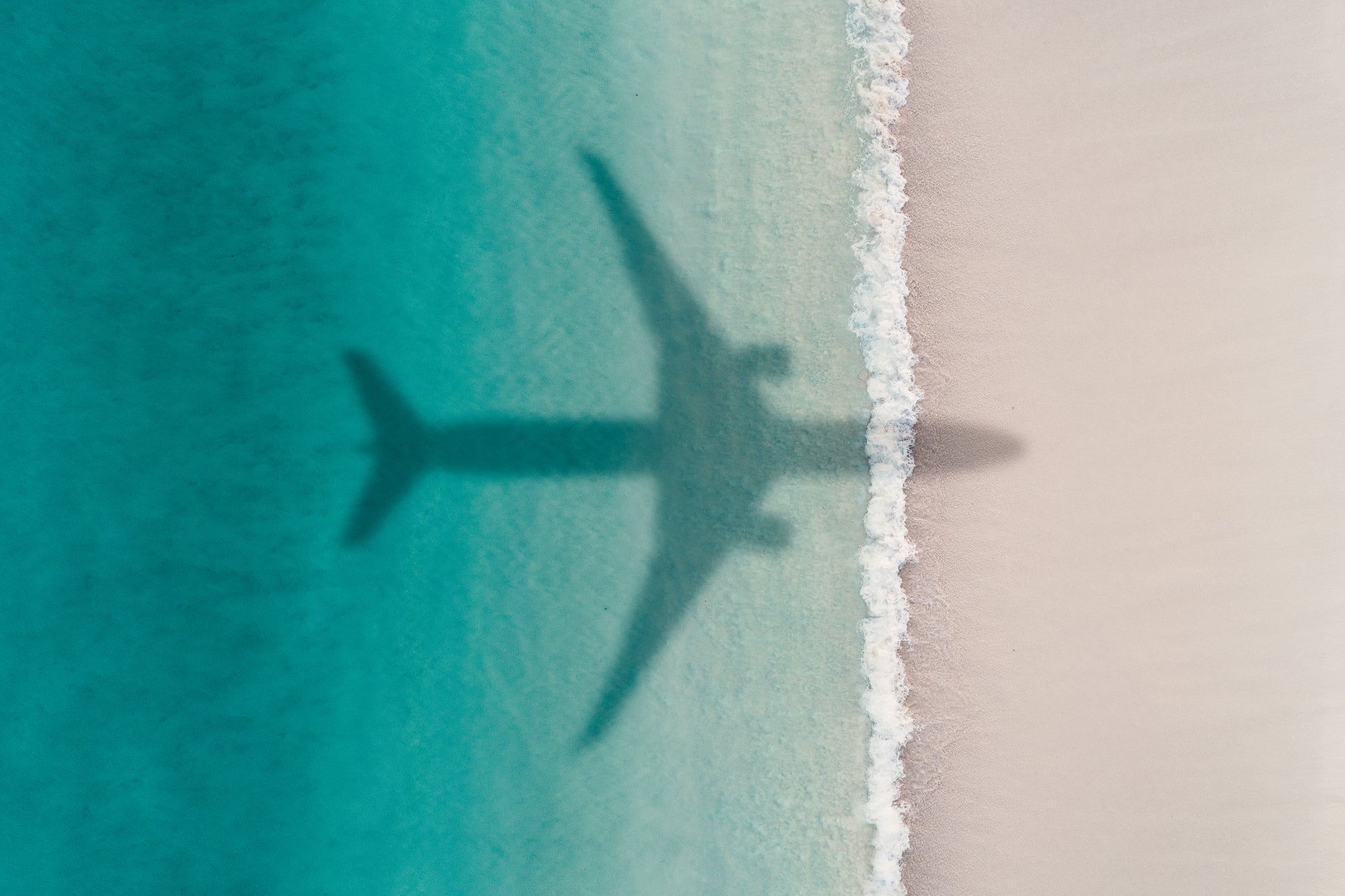 Aerial shot showing an aircraft shadow flying over an idyllic beach scene, Barbados