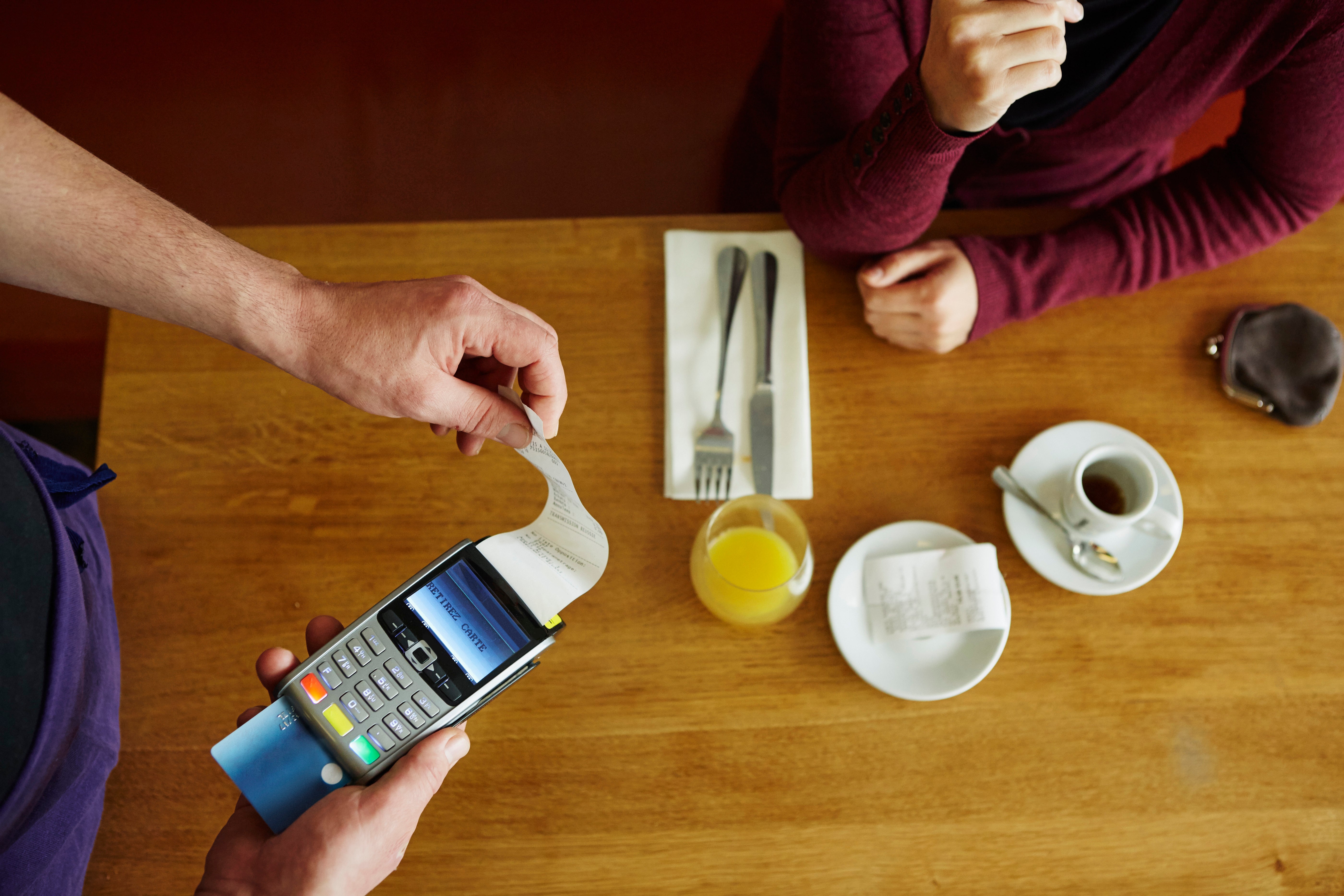 Overhead cropped view of waiter removing receipt from credit card machine in restaurant