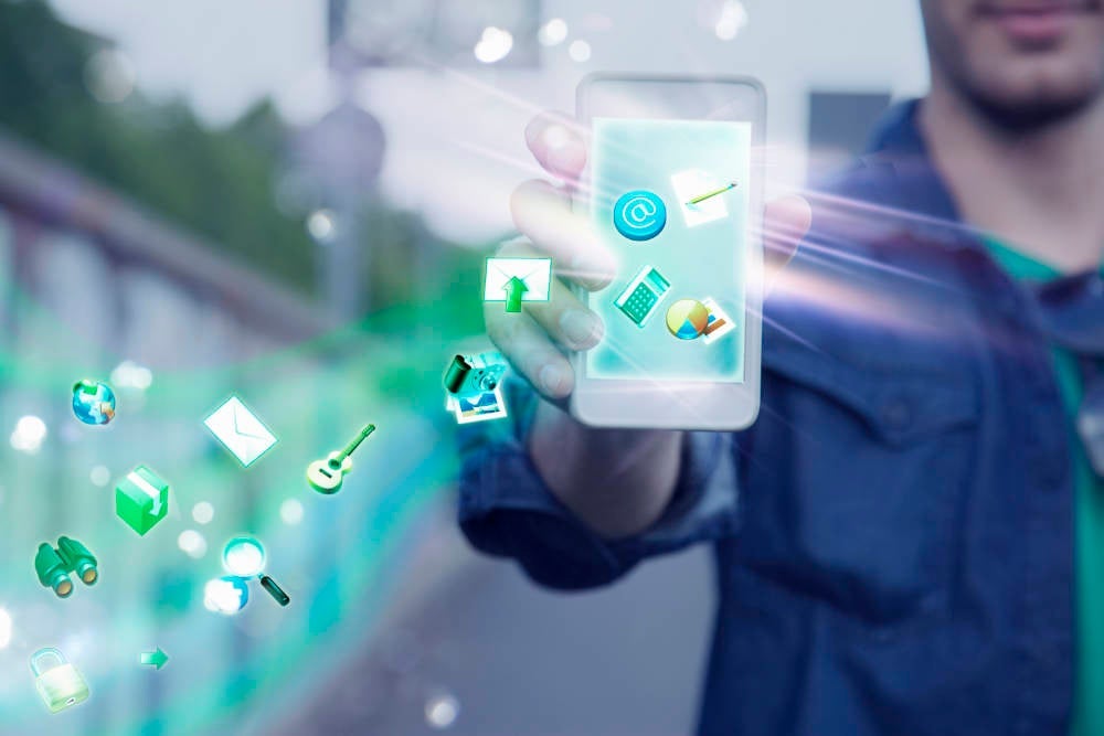Young man holding up smartphone with apps and icons coming out of it