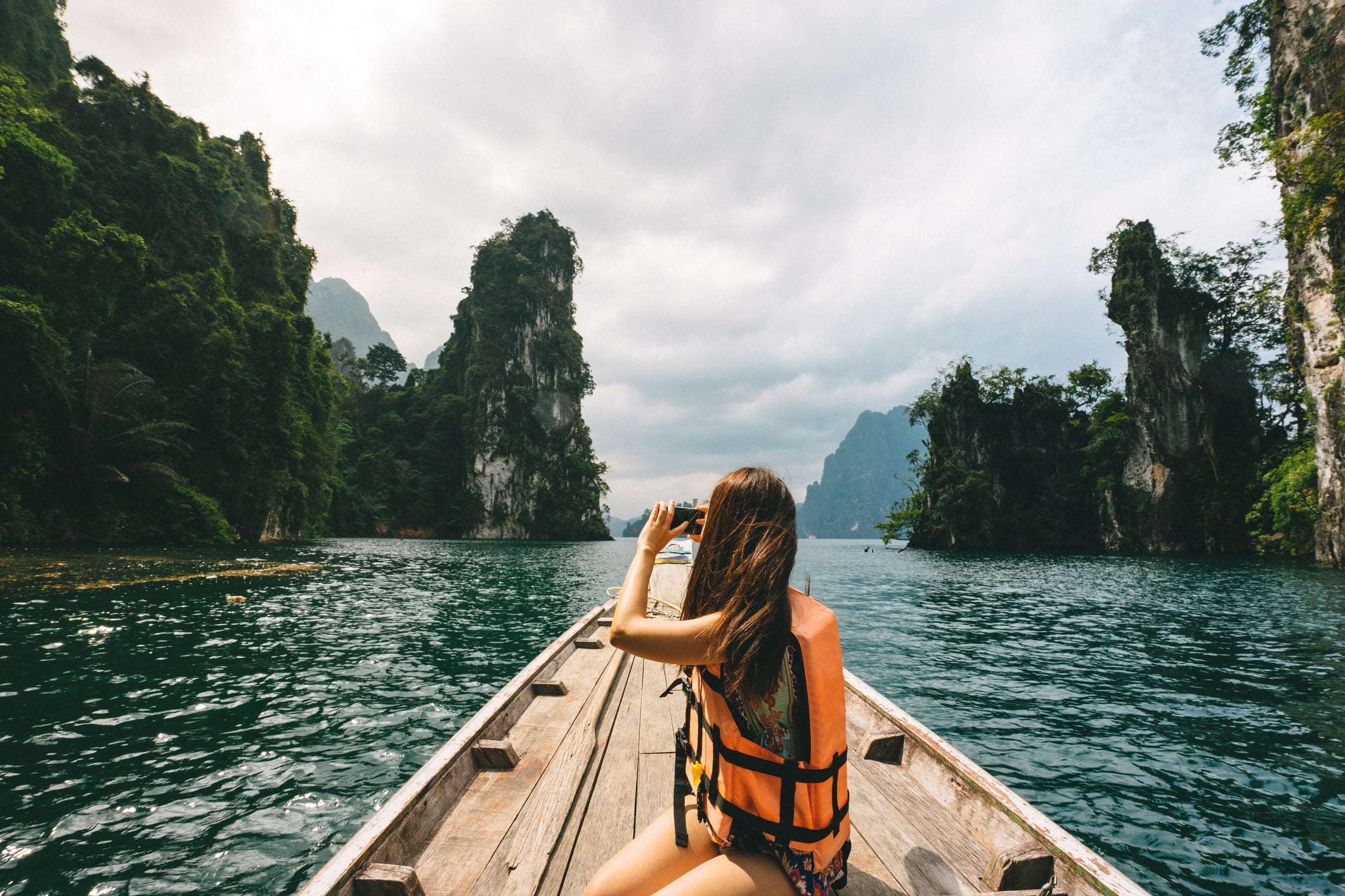 Female tourist exploring lush Jungle lake surrounded by limestone cliffs, Khao Sok National Park, Thailand