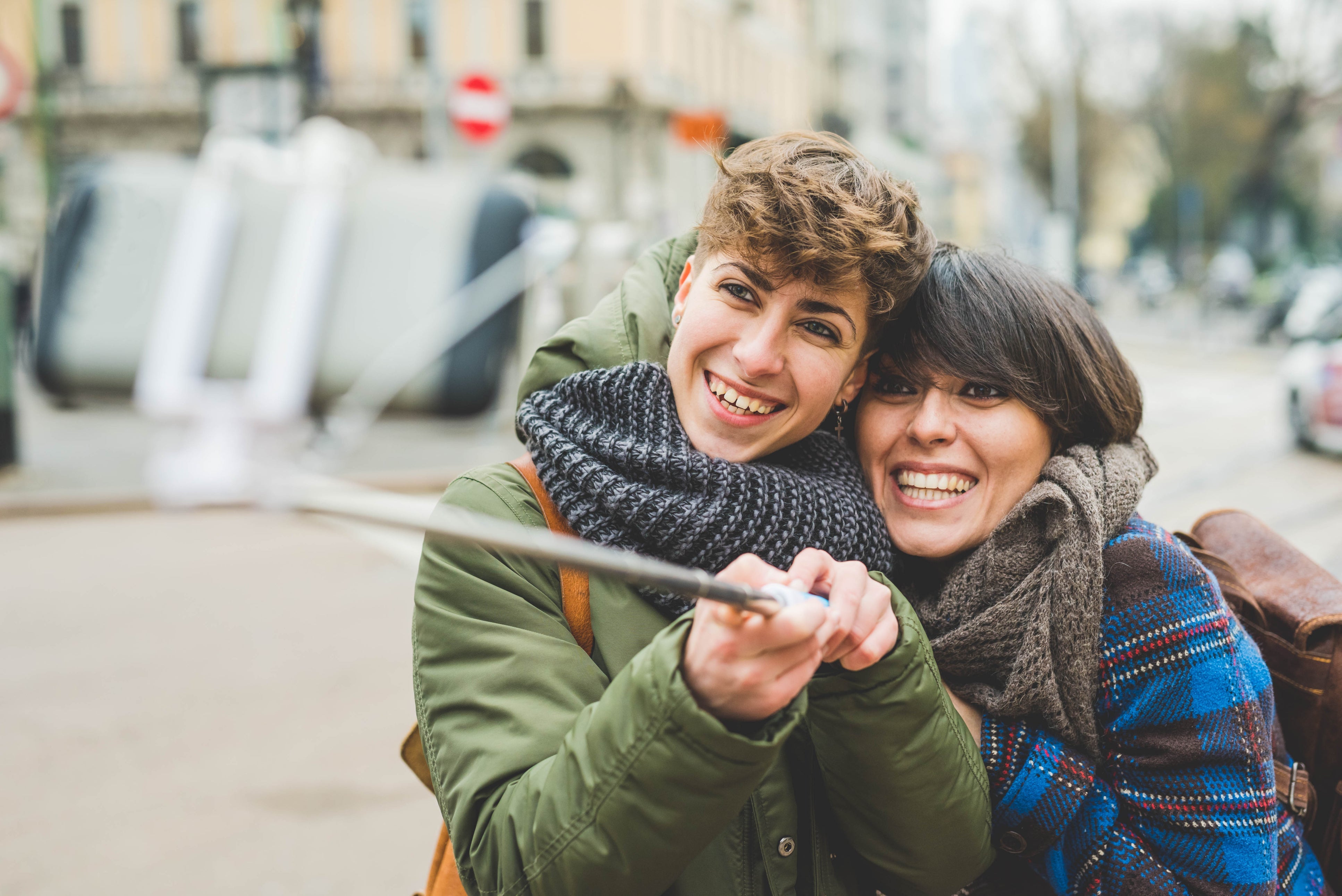 Two sisters, taking self portrait using selfie stick, outdoors