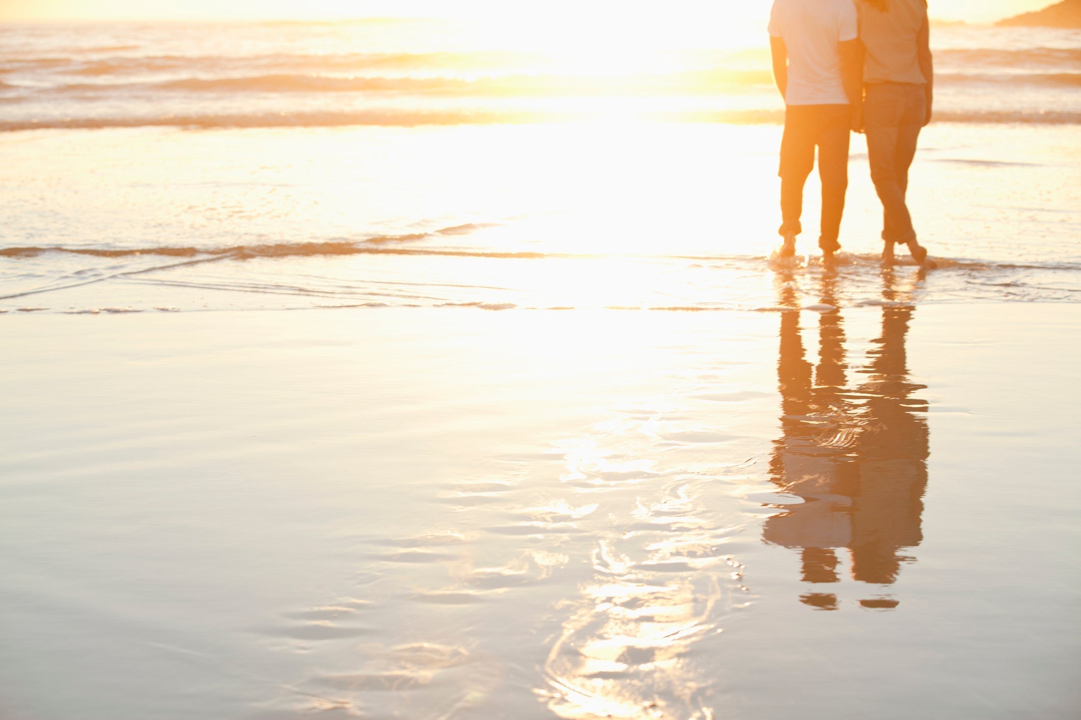 Rear view of a couple standing together on beach at sunset