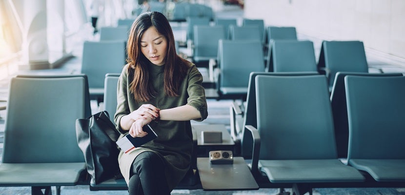 Young businesswoman holding passport and boarding pass on hand, checking wristwatch in airport