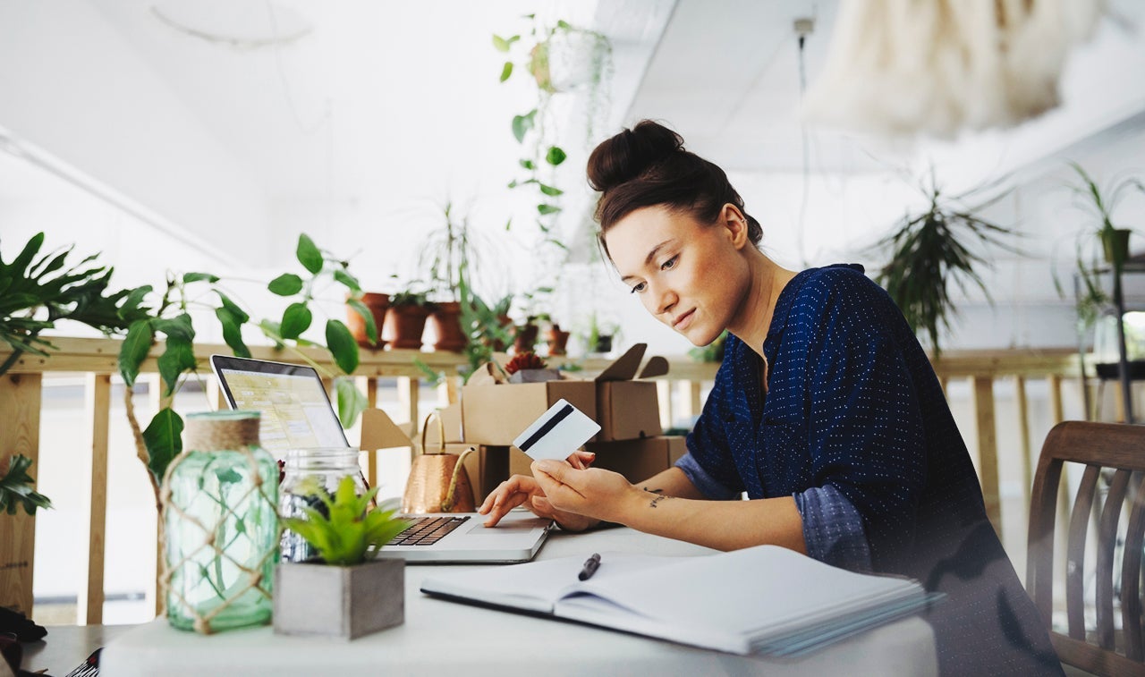 Female plant shop owner with credit card paying bills online at laptop in workshop