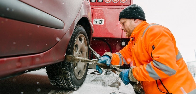 Side view of driver attaching car tire with equipment on tow truck