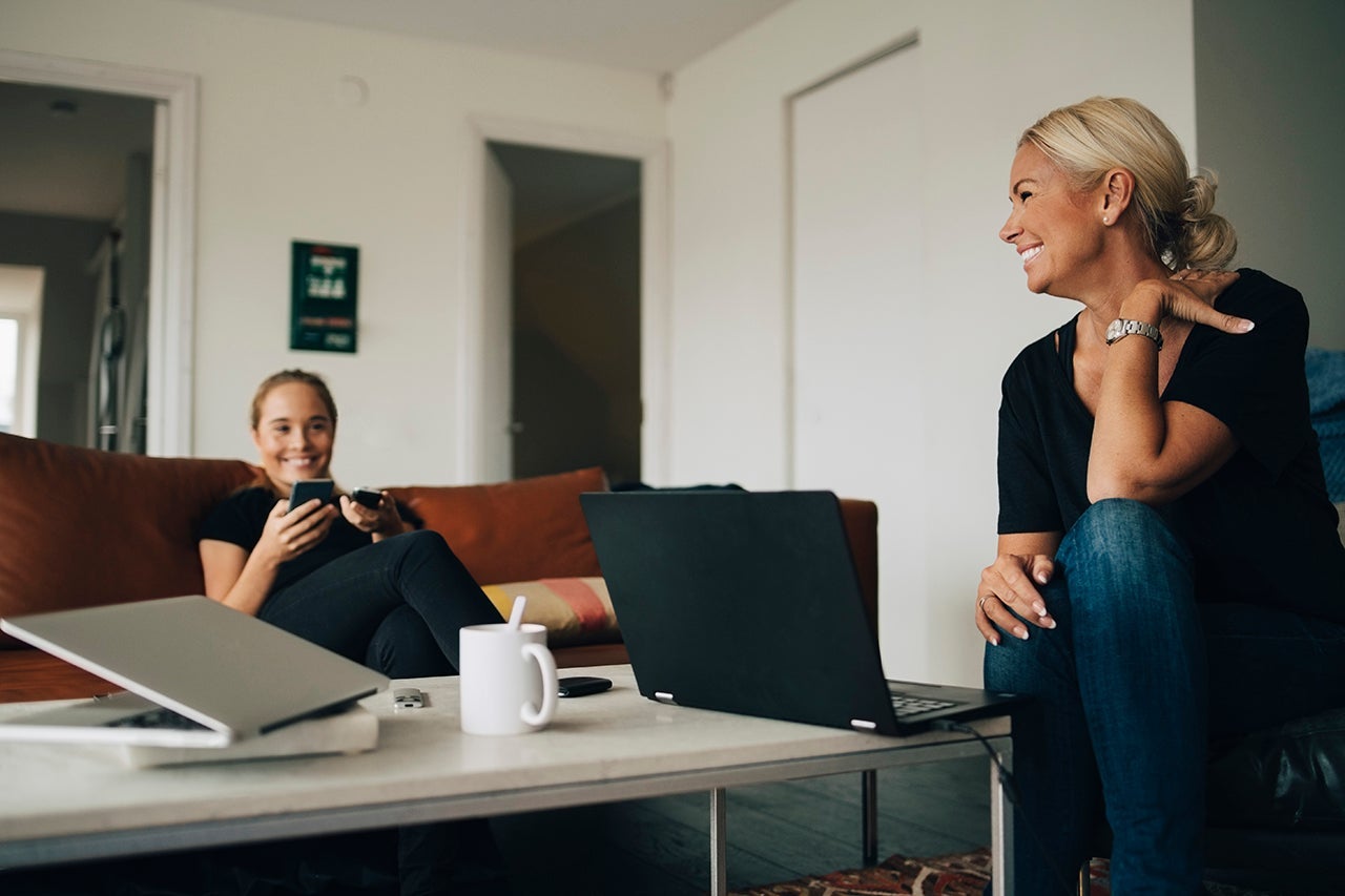 Smiling teenage girl and mother sitting with laptops on coffee table in living room at home
