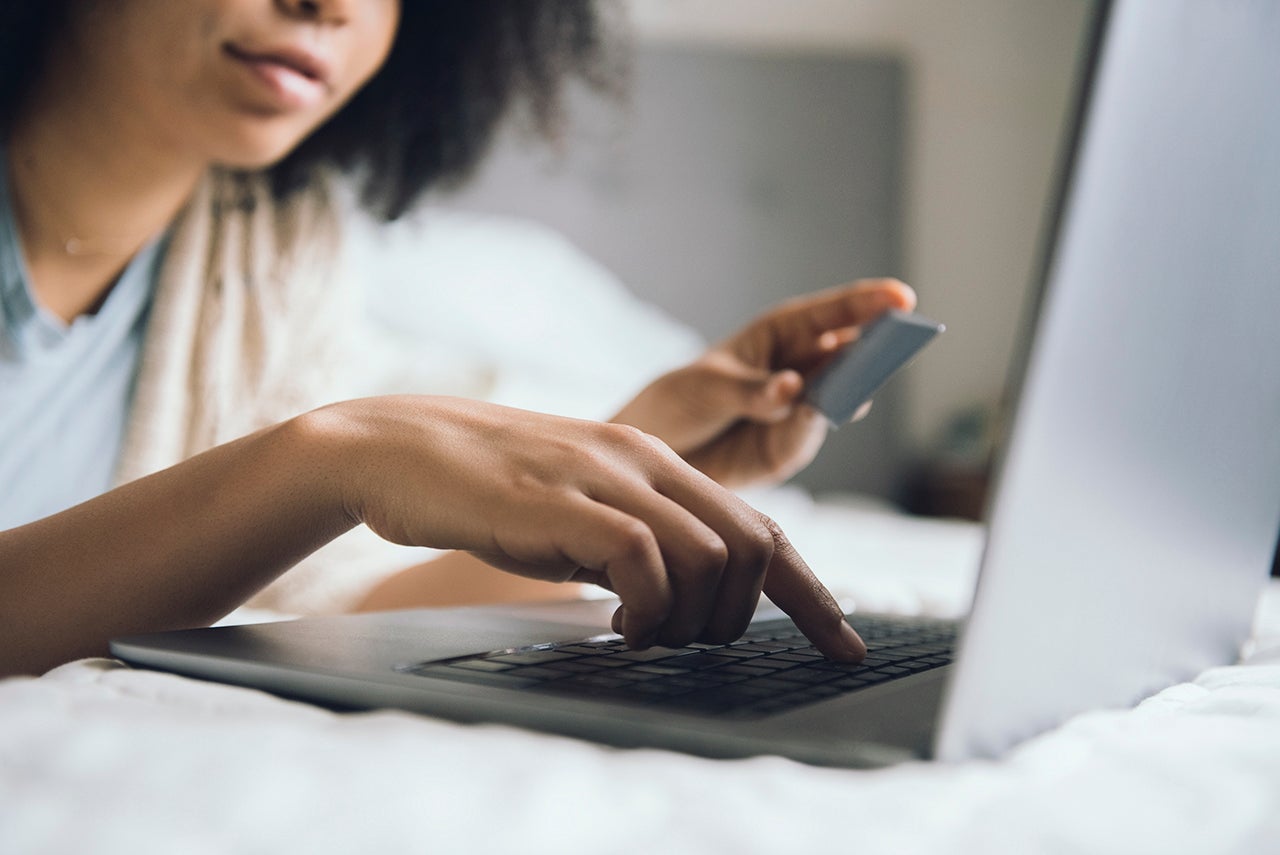 African American woman laying in bed online shopping with laptop