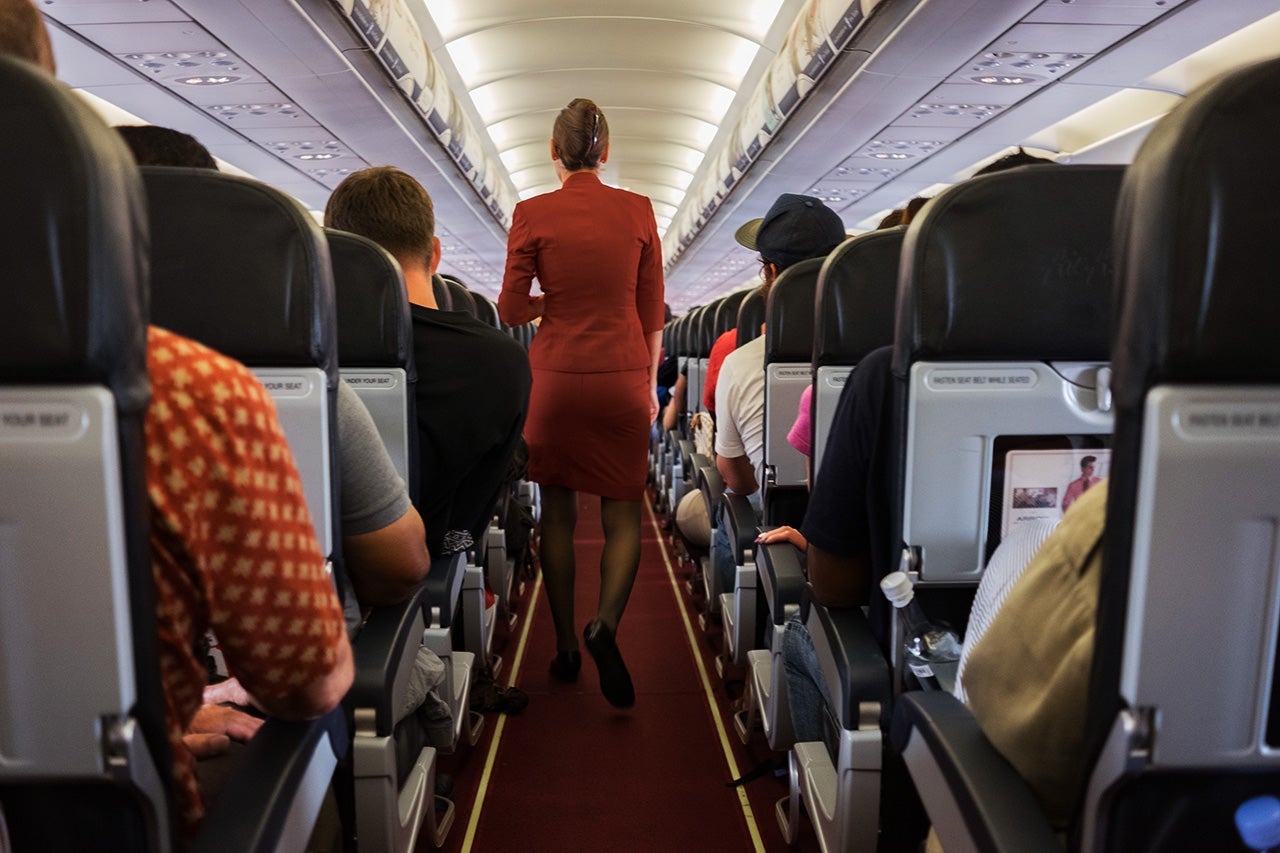 Female cabin crew walks away down aircraft cabin isle