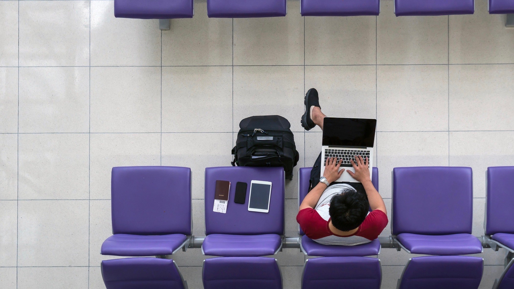 freelanace and travel concept, Happy Asian man traveler working with technology laptop with suitcase, tablet, smart mobile phone and passport at the seat while waiting airplane depart at the airport