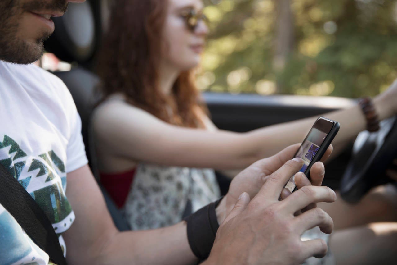 Couple driving and using smart phone in car, enjoying road trip