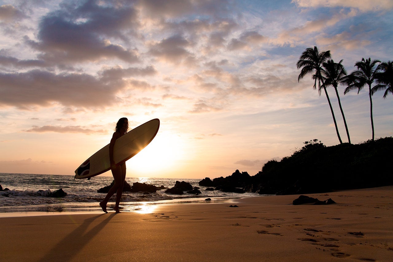 Surfer at sunet walkinh on sand