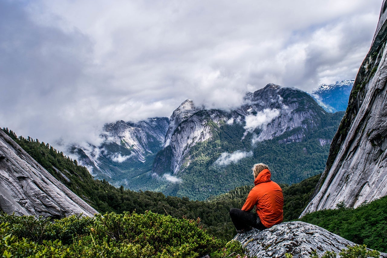 Rear View Of Male Hiker Sitting On Mountain Against Cloudy Sky
