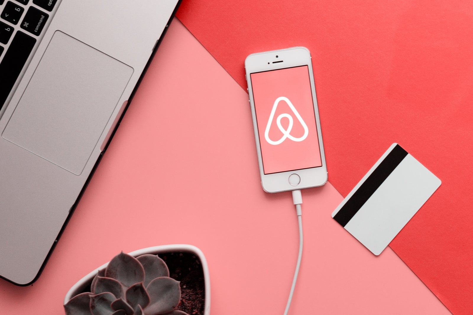 MINSK, BELARUS - May 11, 2018: Top view of white Apple Iphone with Airbnb logo on display. Flat lay with credit bank card, laptop, succulent plant and smartphone on the pink and coral table as background.