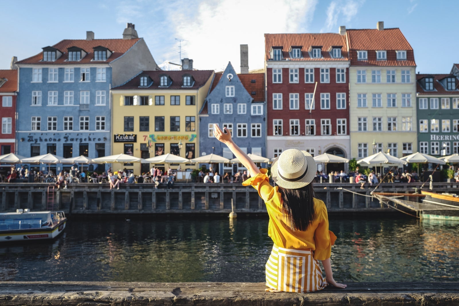 Young woman sitting in front of colorful buildings along Nyhavn (New Harbour), Copenhagen, Denmark