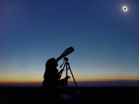 Young woman observing total solar eclipse in Mar 29, 2006 through binoculars.