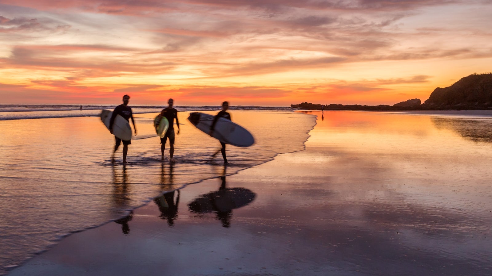 Surfers at sunset walking on beach, Costa Rica