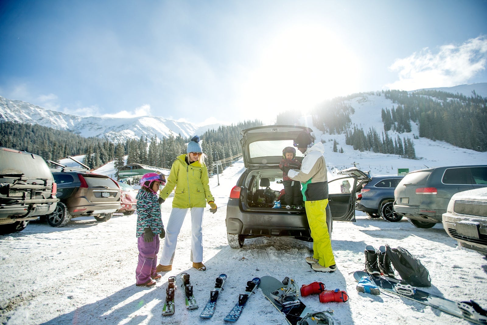 Mixed race family at a parking lot unloading ski and snowboard equipment out of their car and getting the kids ready for a day on the mountain.