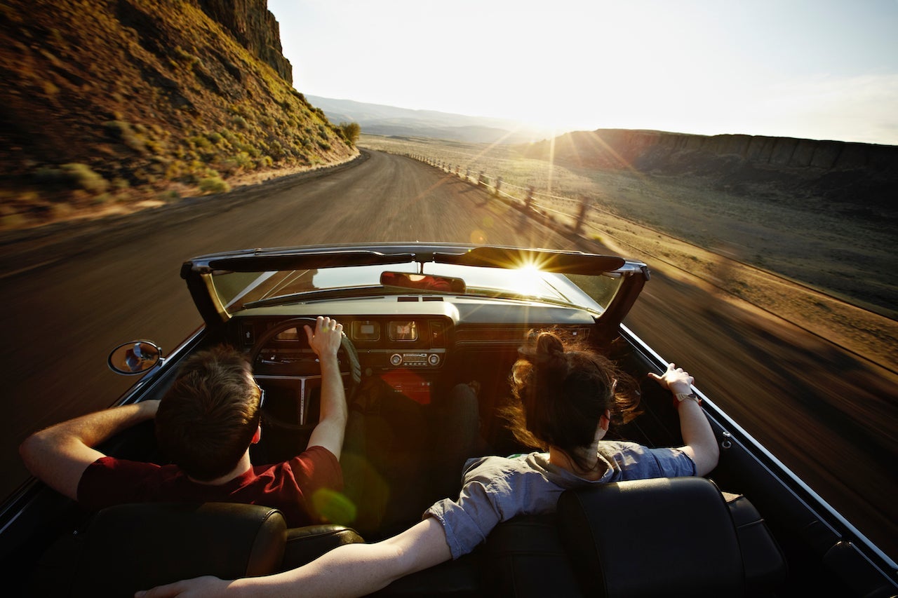Young couple driving convertible at sunset