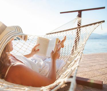 Young woman, reading a book in a hammock at sunset.