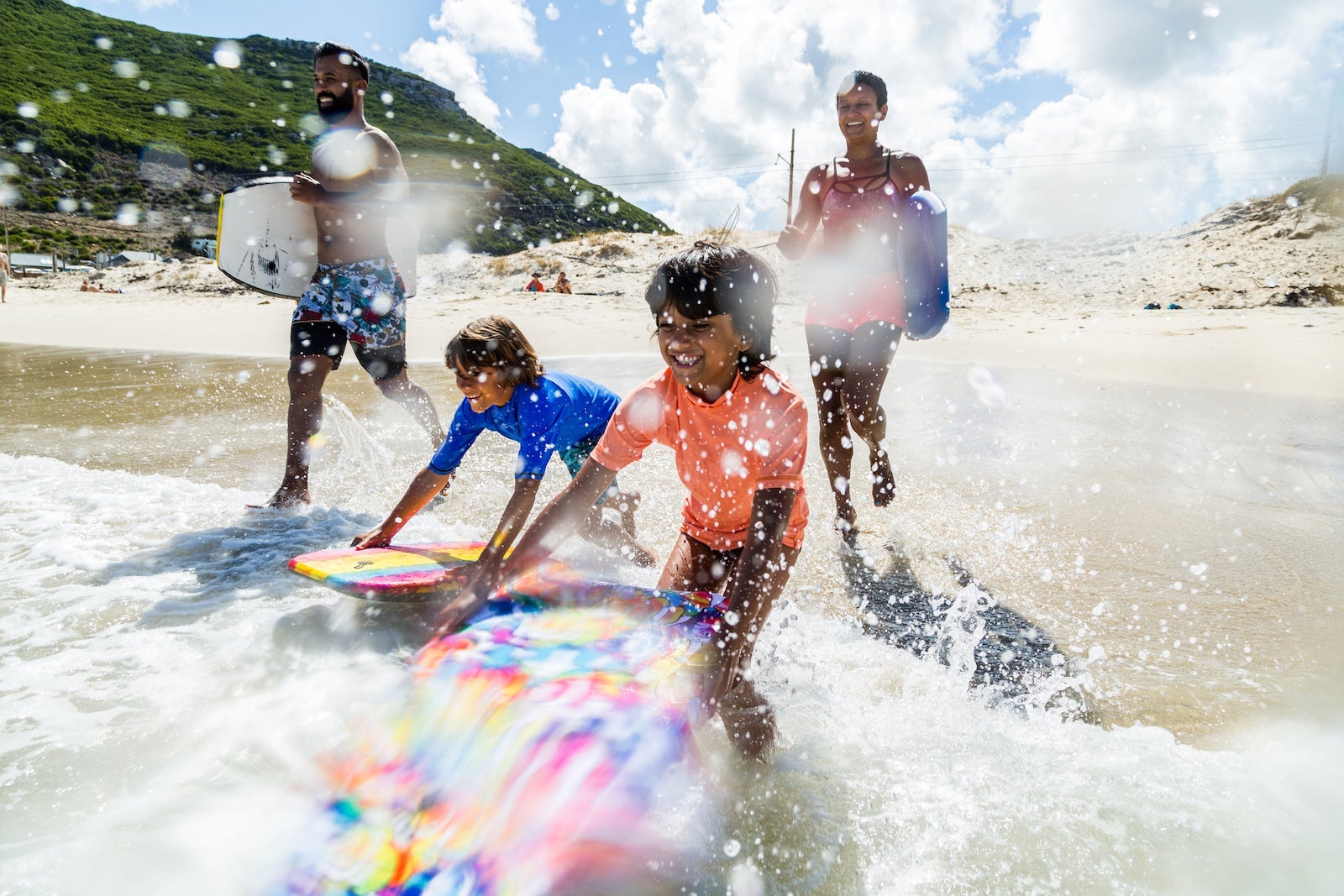 Family running and splashing into sea together with body boards