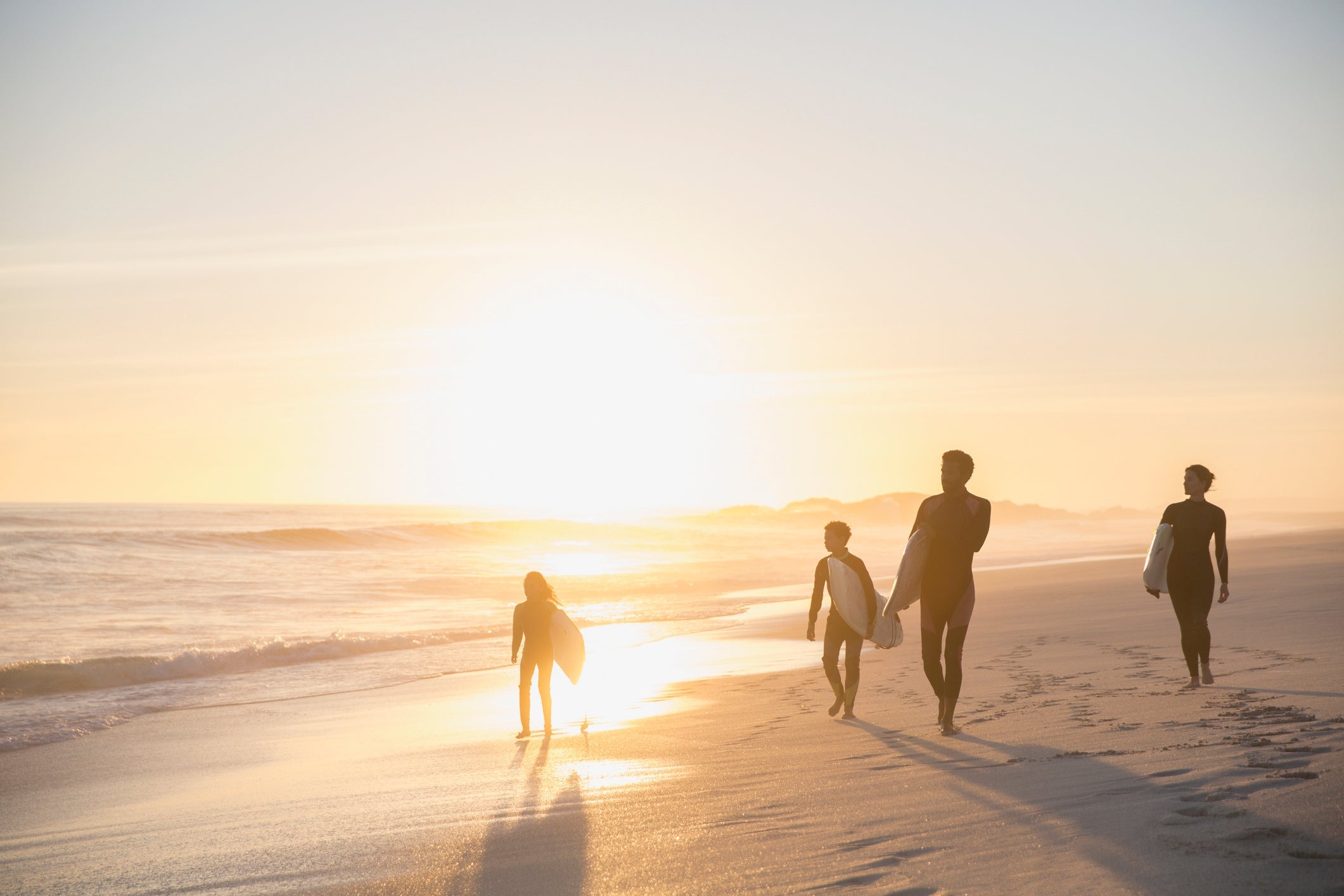 Silhouette family surfers walking with surfboards on idyllic, sunny summer sunset beach