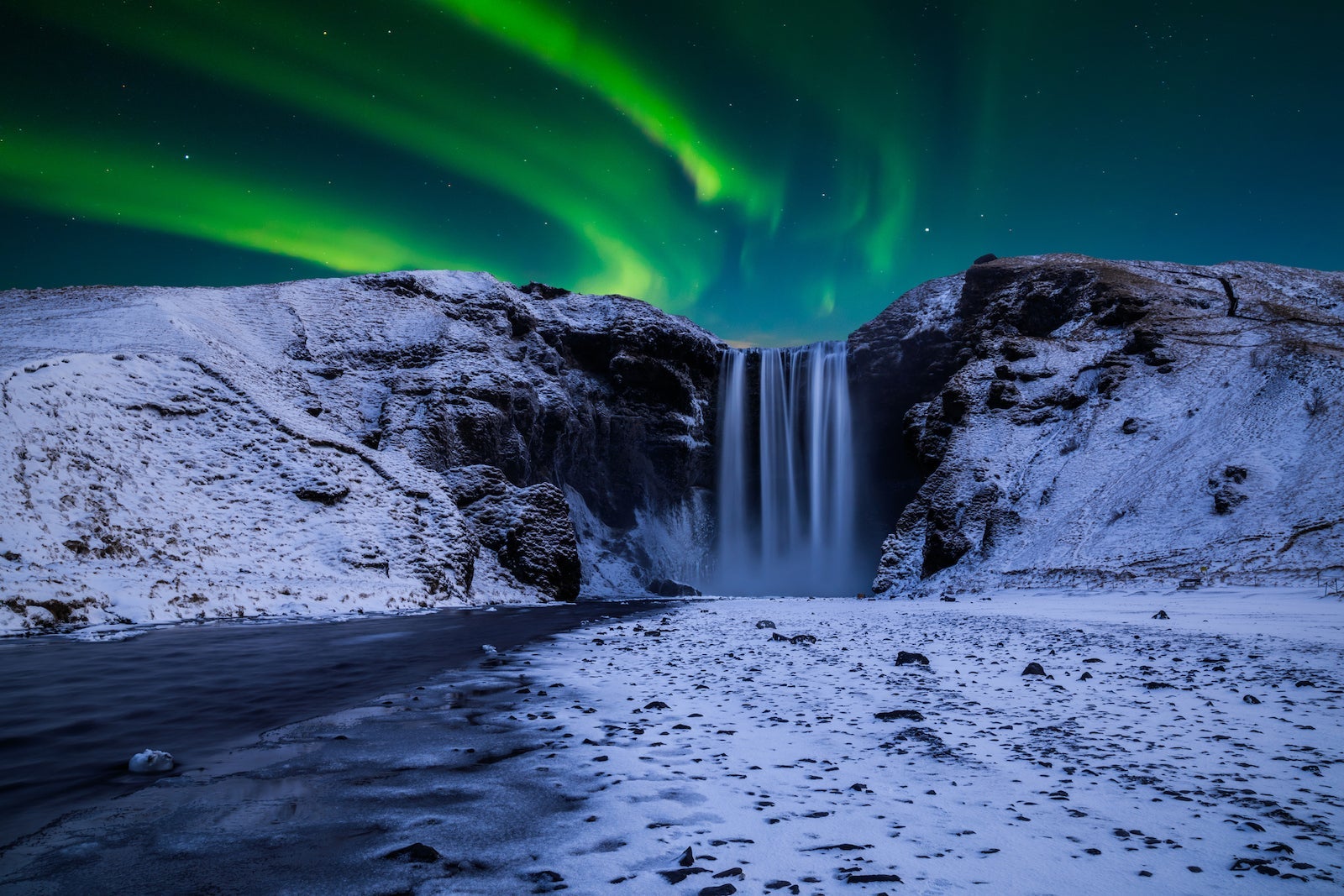 Skogafoss waterfall in the winter at night under the northern lights. Iceland