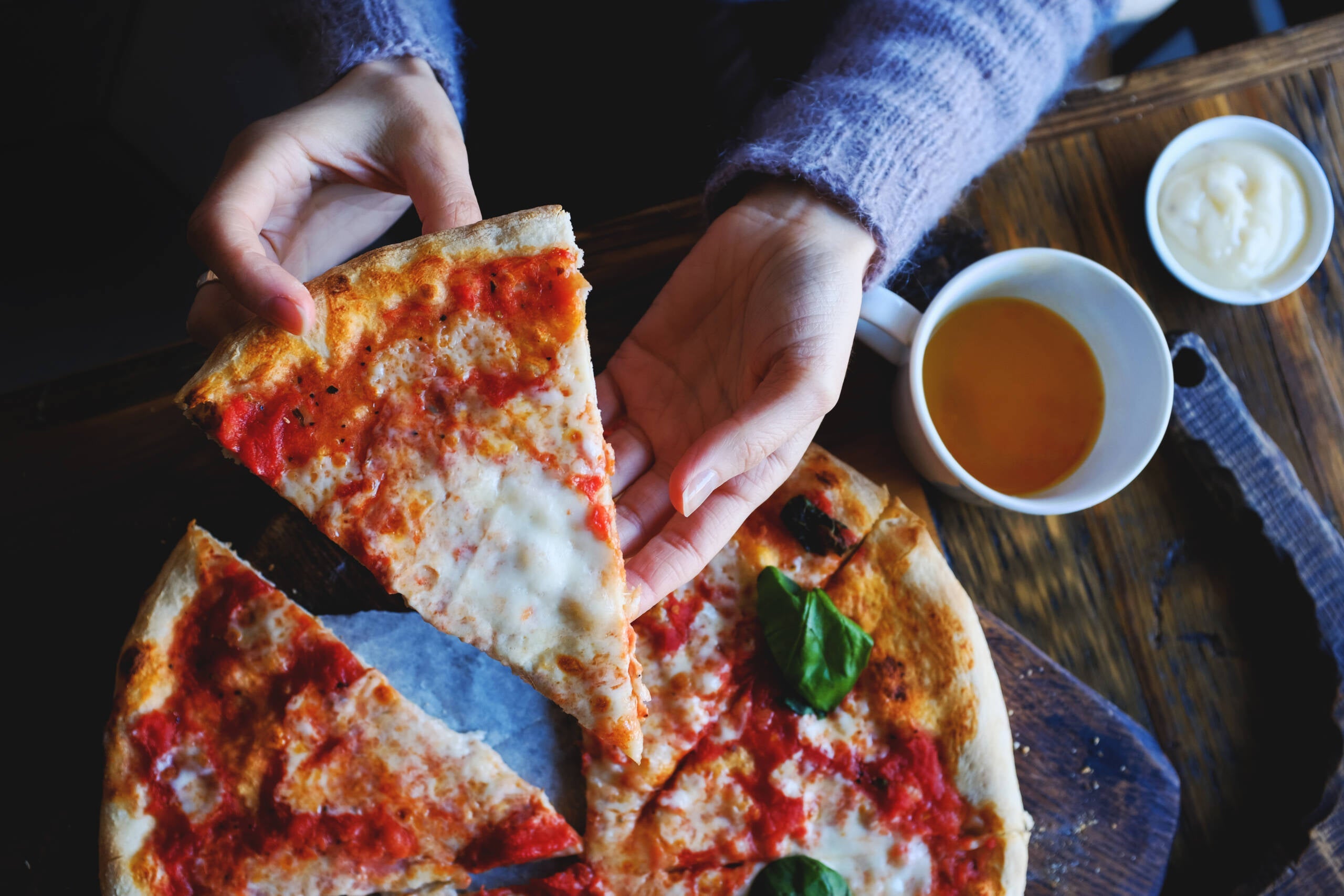 The girl takes a piece of vegetarian pizza with mozzarella cheese, tomatoes, spices and fresh Basil. Delicious Italian food. Sliced pizza Margarita on a wooden Board. Close up. Delicious lunch, snack