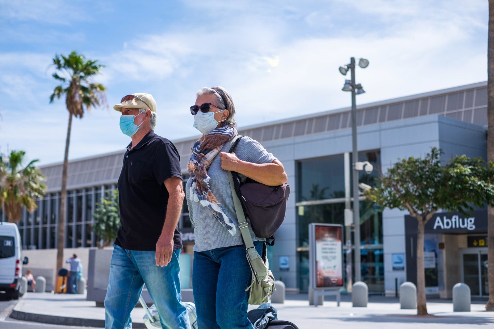 two senior walking with their baggage and wearing medical mask to prevent covid-19 or coronavirus or another type of virus or disease - safe travelers concept and lifestyle walking outdoor