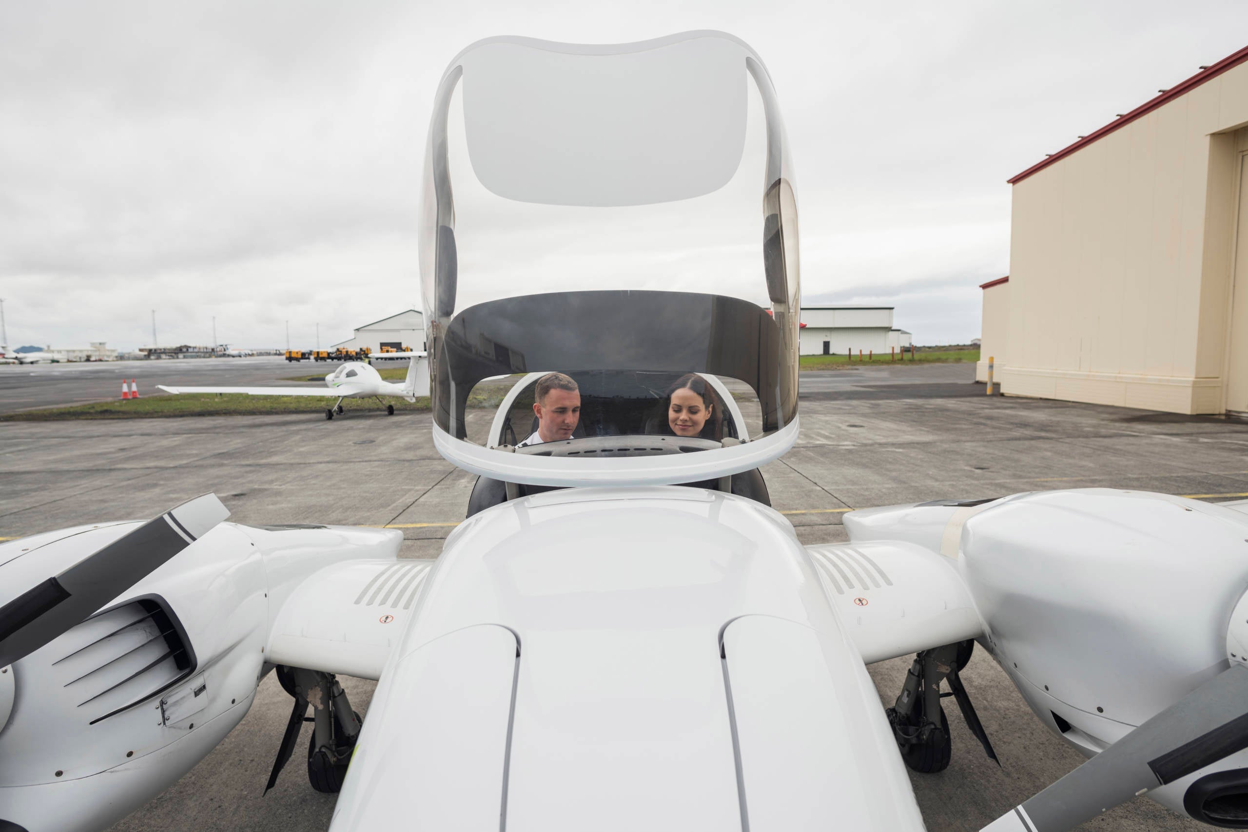 High angle view of male pilot guiding female trainee while sitting in airplane against cloudy sky at airport runway