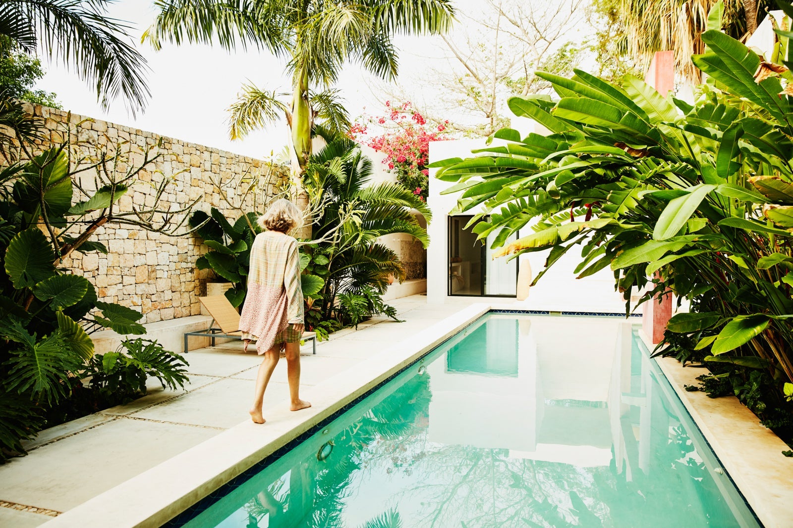 Senior woman walking along edge of pool at tropical spa