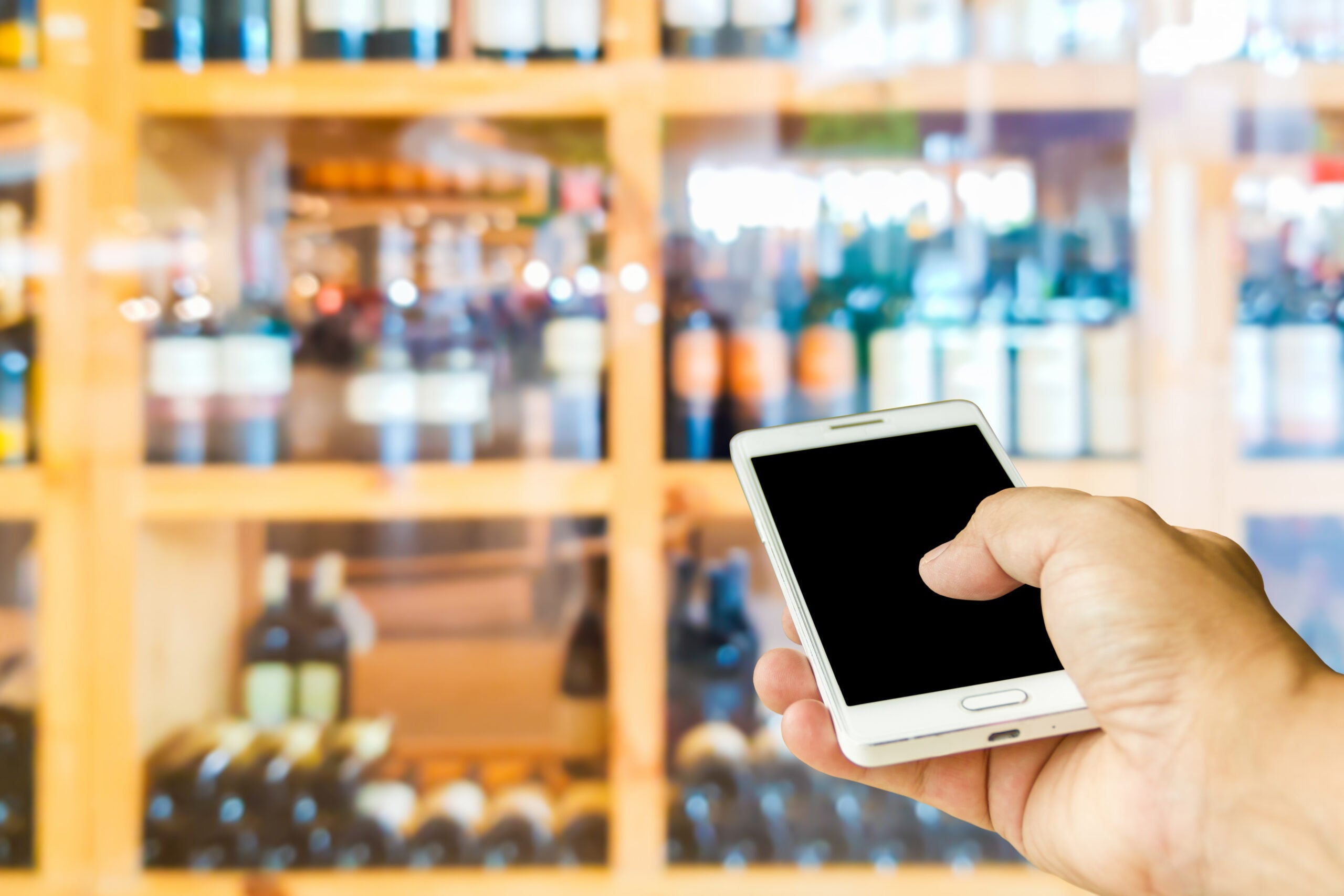 Man,Use,Mobile,Phone,,Blur,Image,Of,Wine,Shop,As