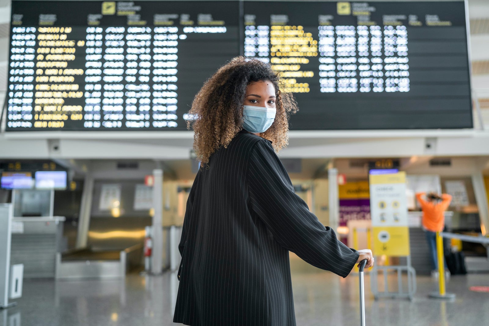Woman wearing protective face mask looking over shoulder while standing at airport