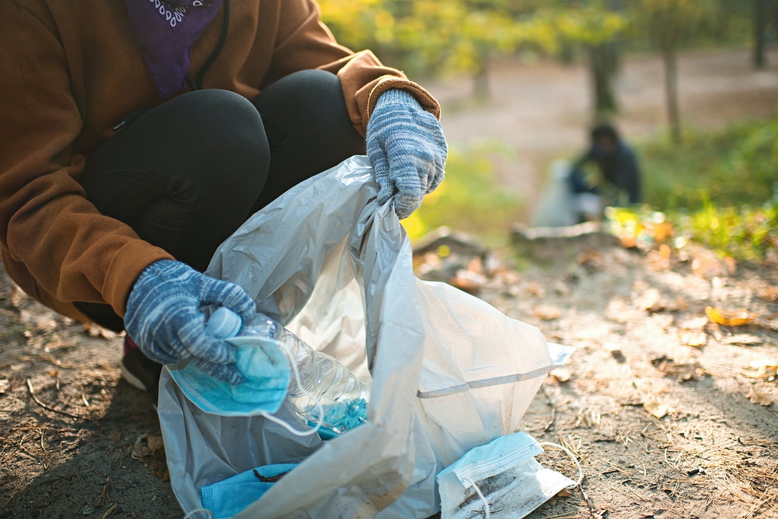 Volunteer girl in alternative face covering bandana cleaning nature from masks and plastic