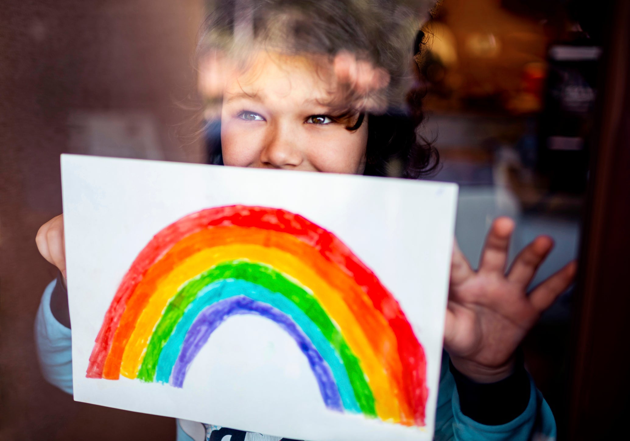 Little boy sticking his rainbow painting on the window
