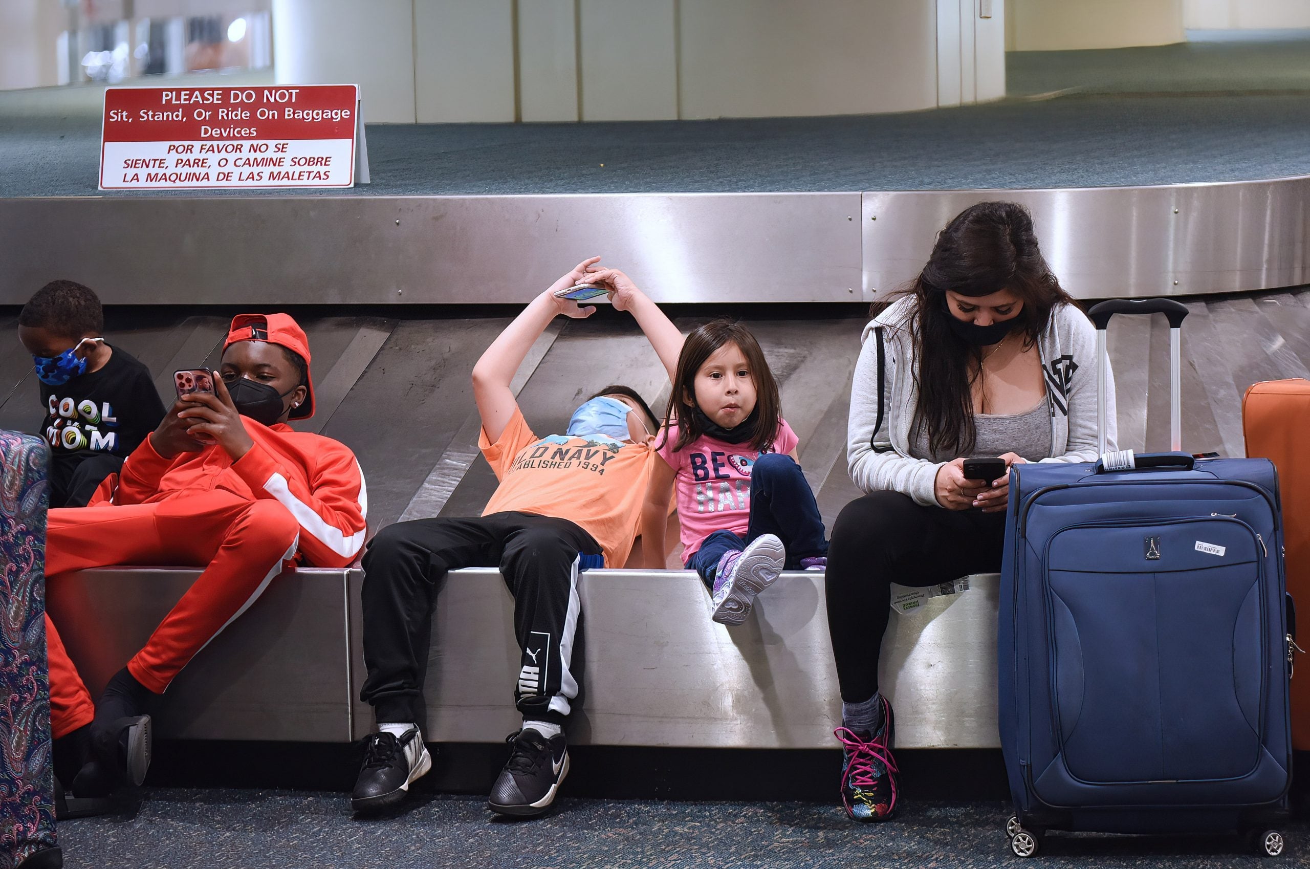 Young travelers sit on a baggage carousel after arriving at
