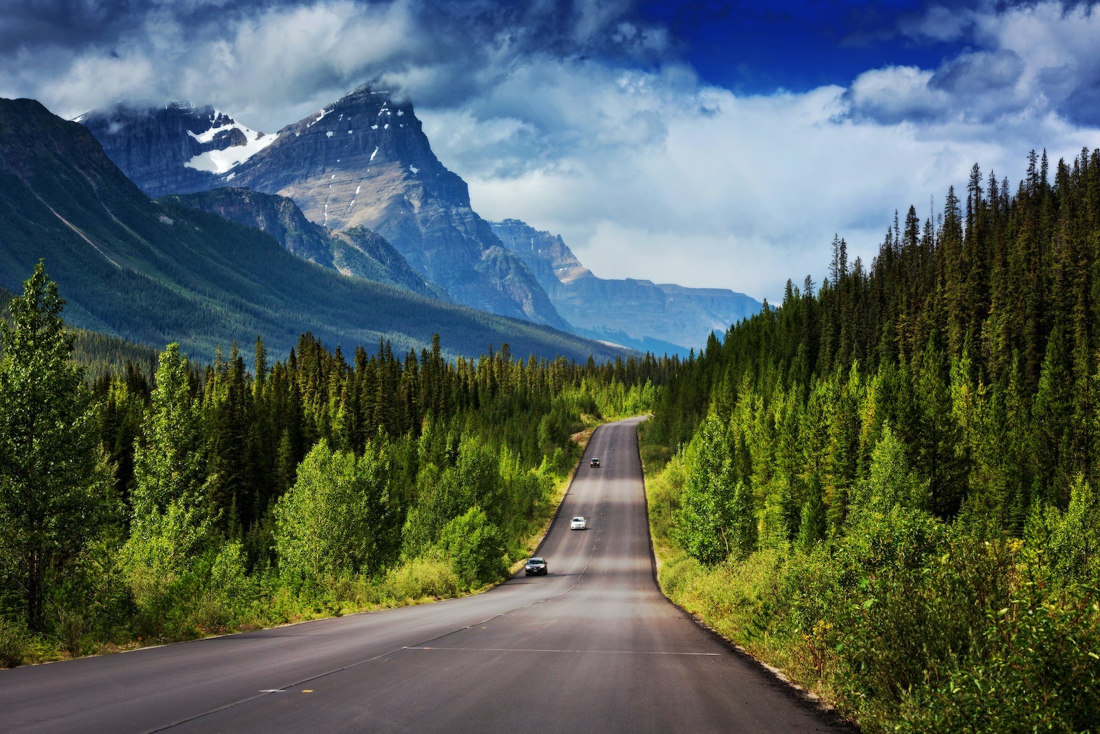 Two-lane famous Icefields Parkway between Lake Louise and Jasper, Alberta, with snowcapped mountains looming above in summer