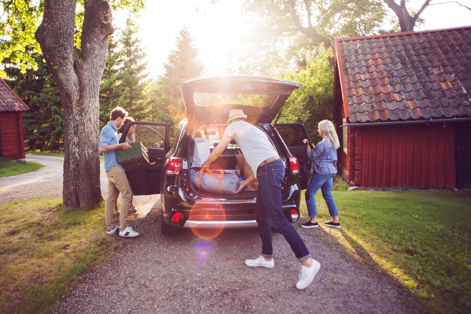 Full length of friends loading luggage into car on road during sunny day