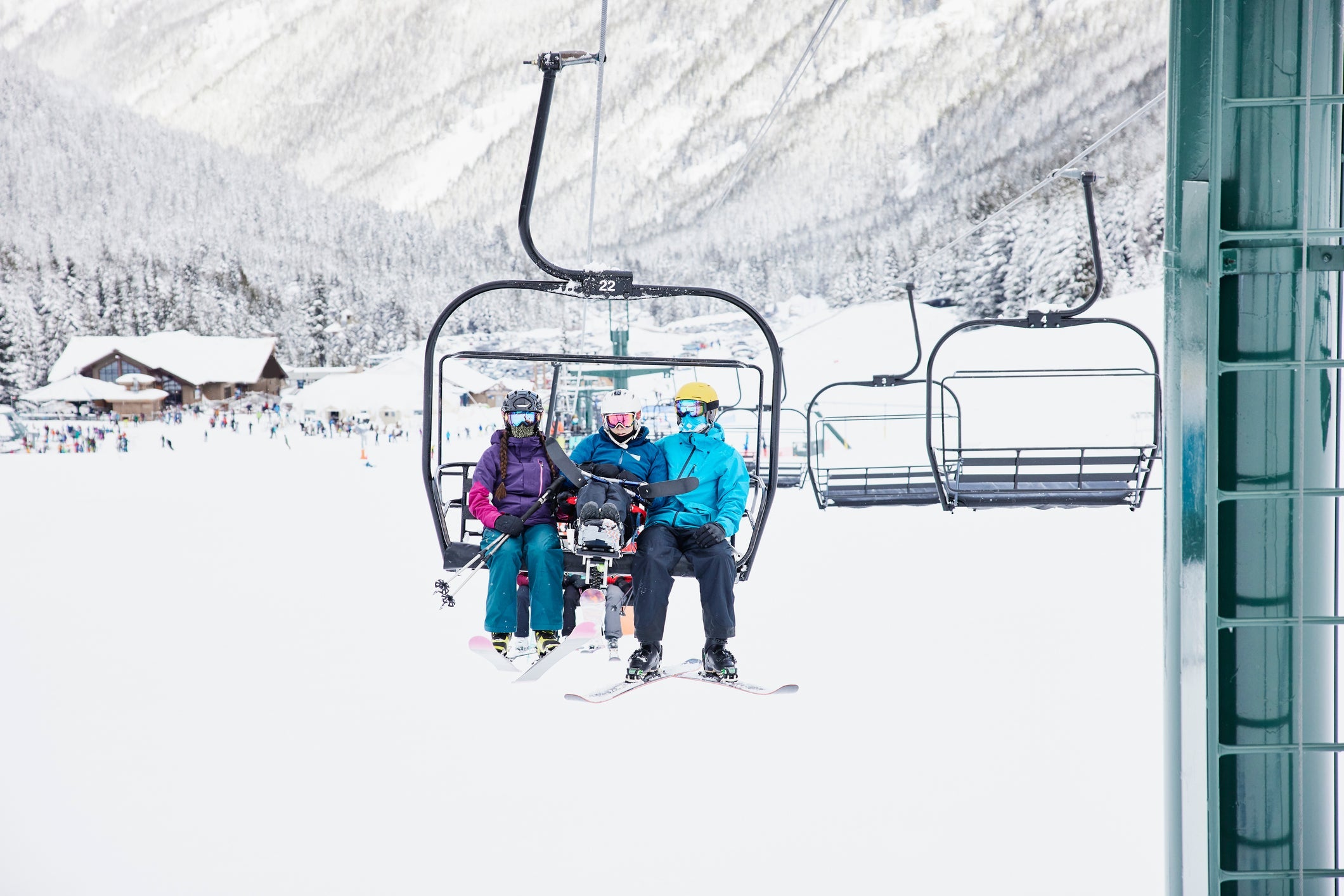 Wide view of female adaptive athlete riding chairlift with friends while skiing at resort on winter morning