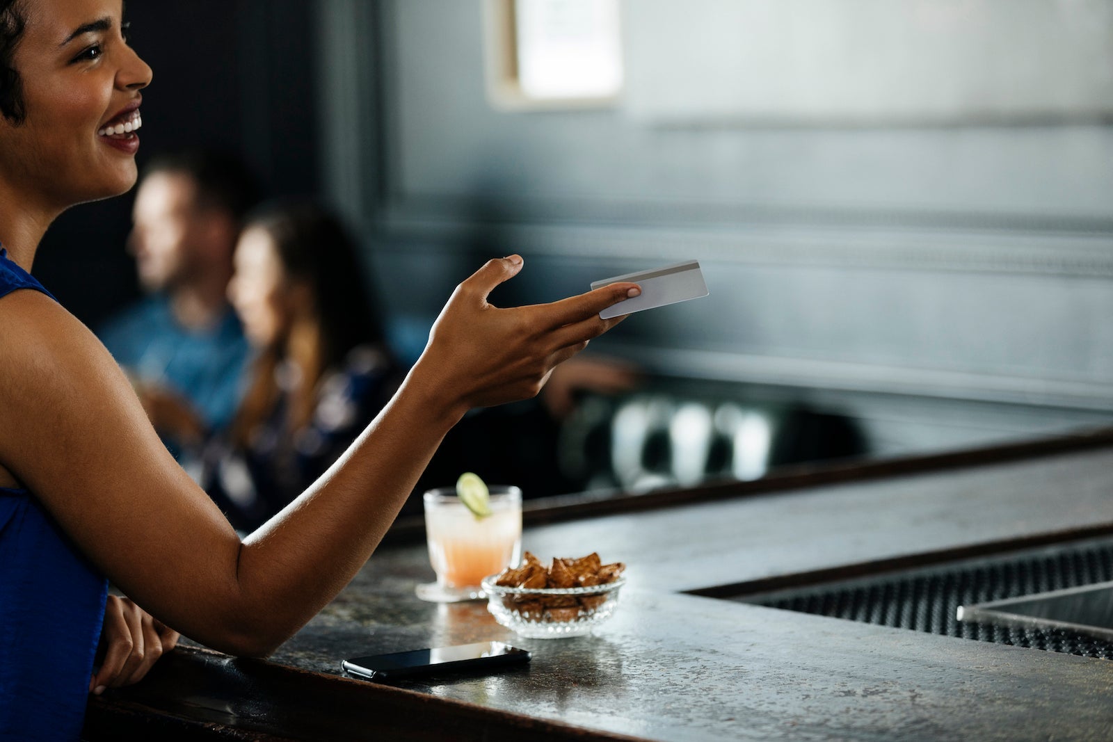 Smiling woman giving credit card at bar counter in restaurant