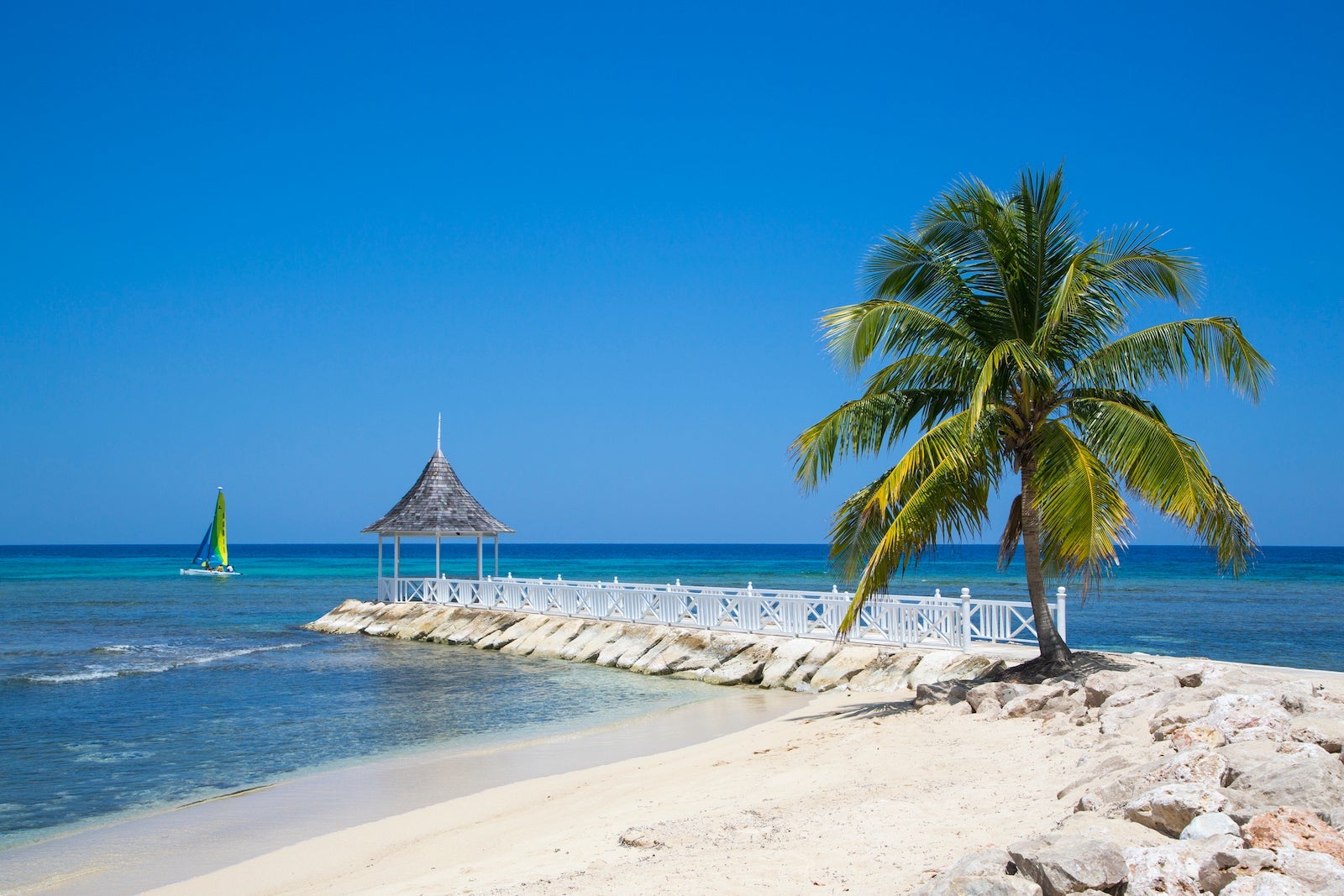 Palm tree, beach and pavillion at Half Moon Resort. Palm tree at Sunset Beach, jetty with pavillion and Hobie Cat sailboat at Half Moon Resort, Rose Hall, near Montego Bay, Saint James, Jamaica
