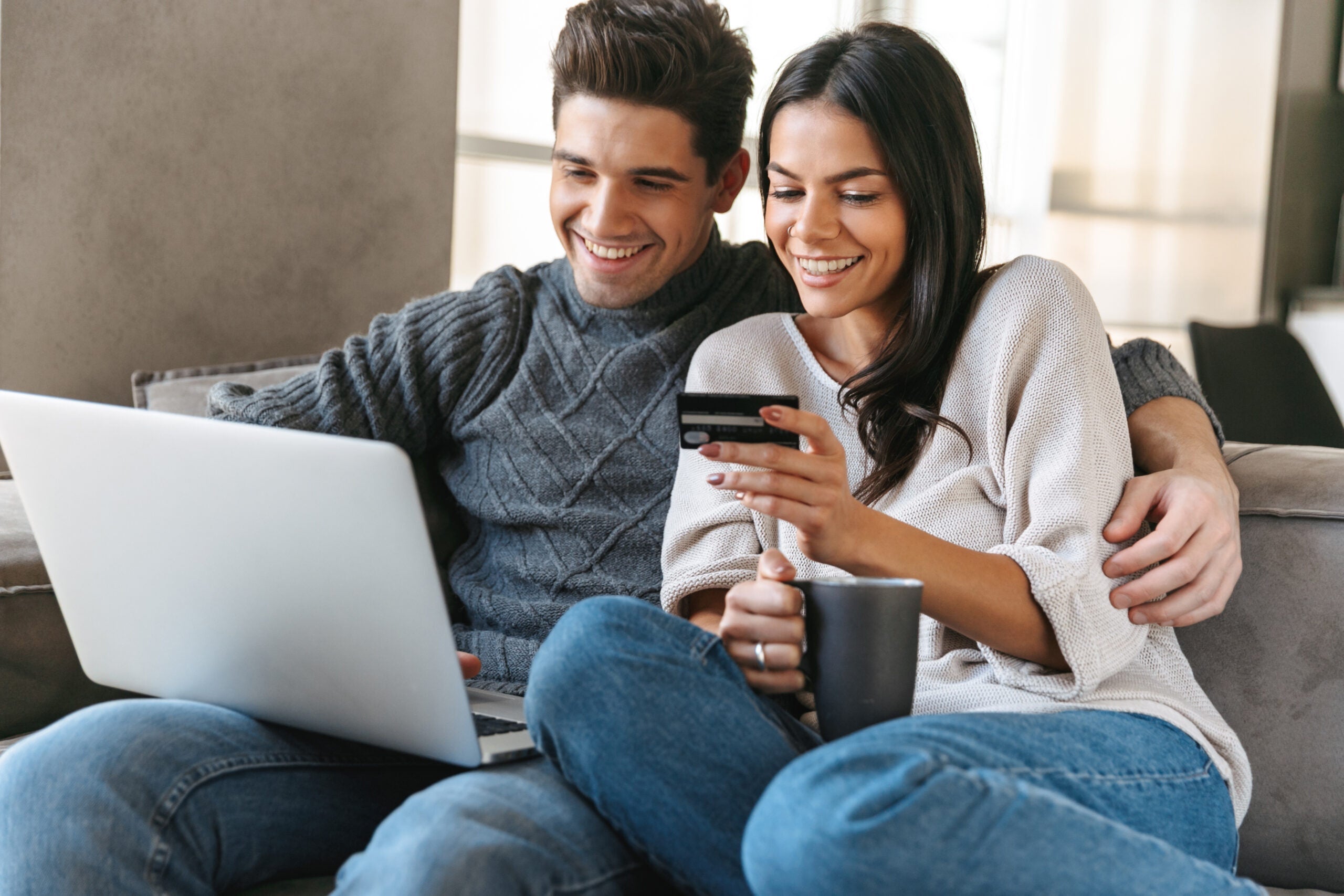 Happy,Young,Couple,Sitting,On,A,Couch,At,Home,,Using