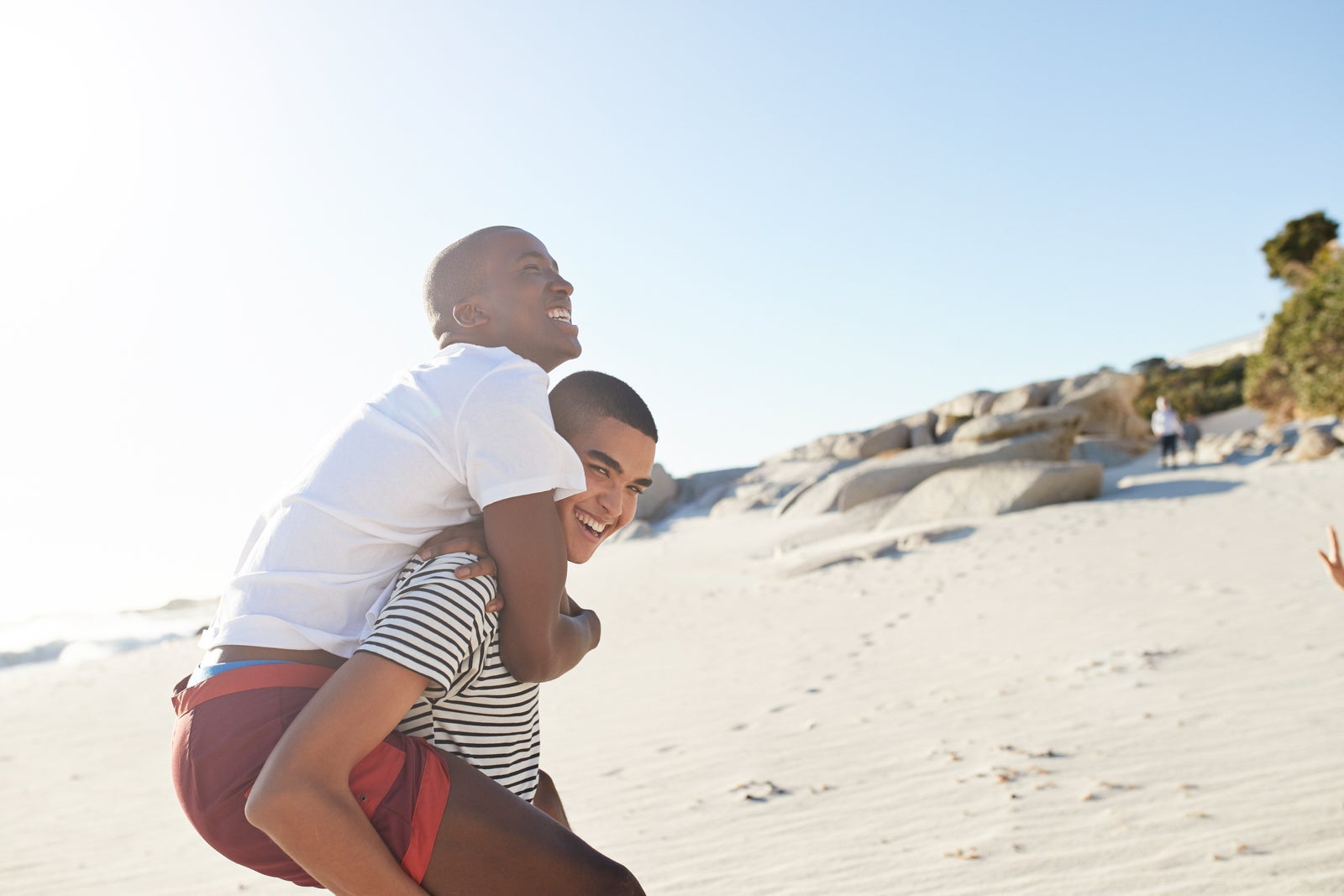 Happy man piggybacking friend on sandy beach