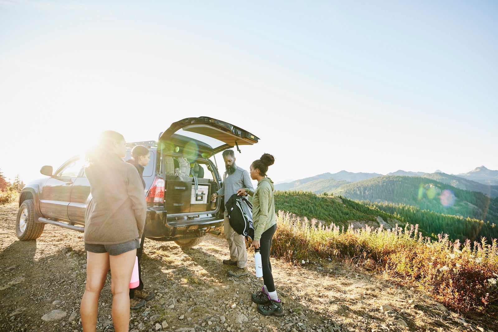 Father and daughters preparing to begin backpacking trip at back of car