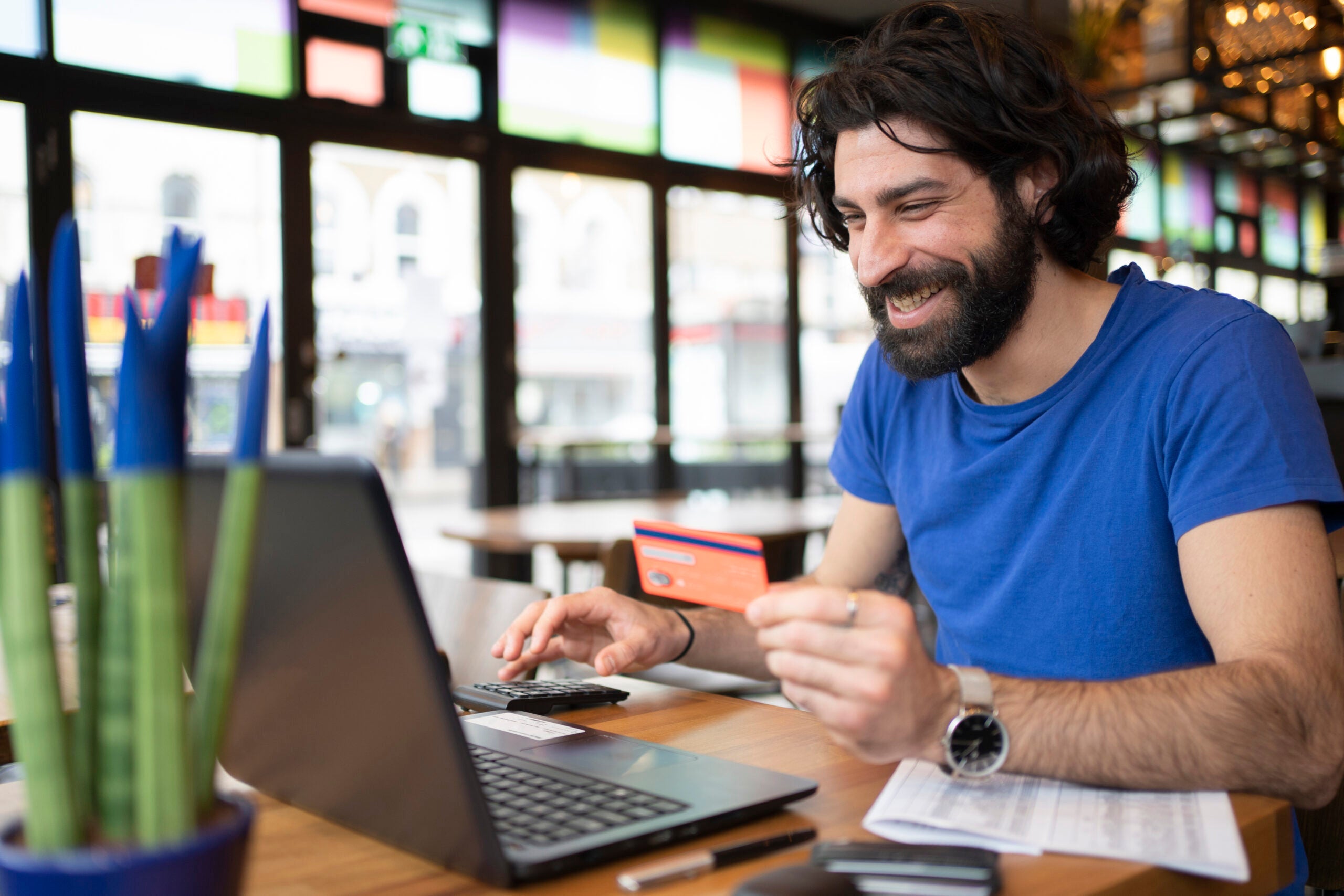 Smiling businessman doing online shopping holding credit card in front of laptop at coworking office