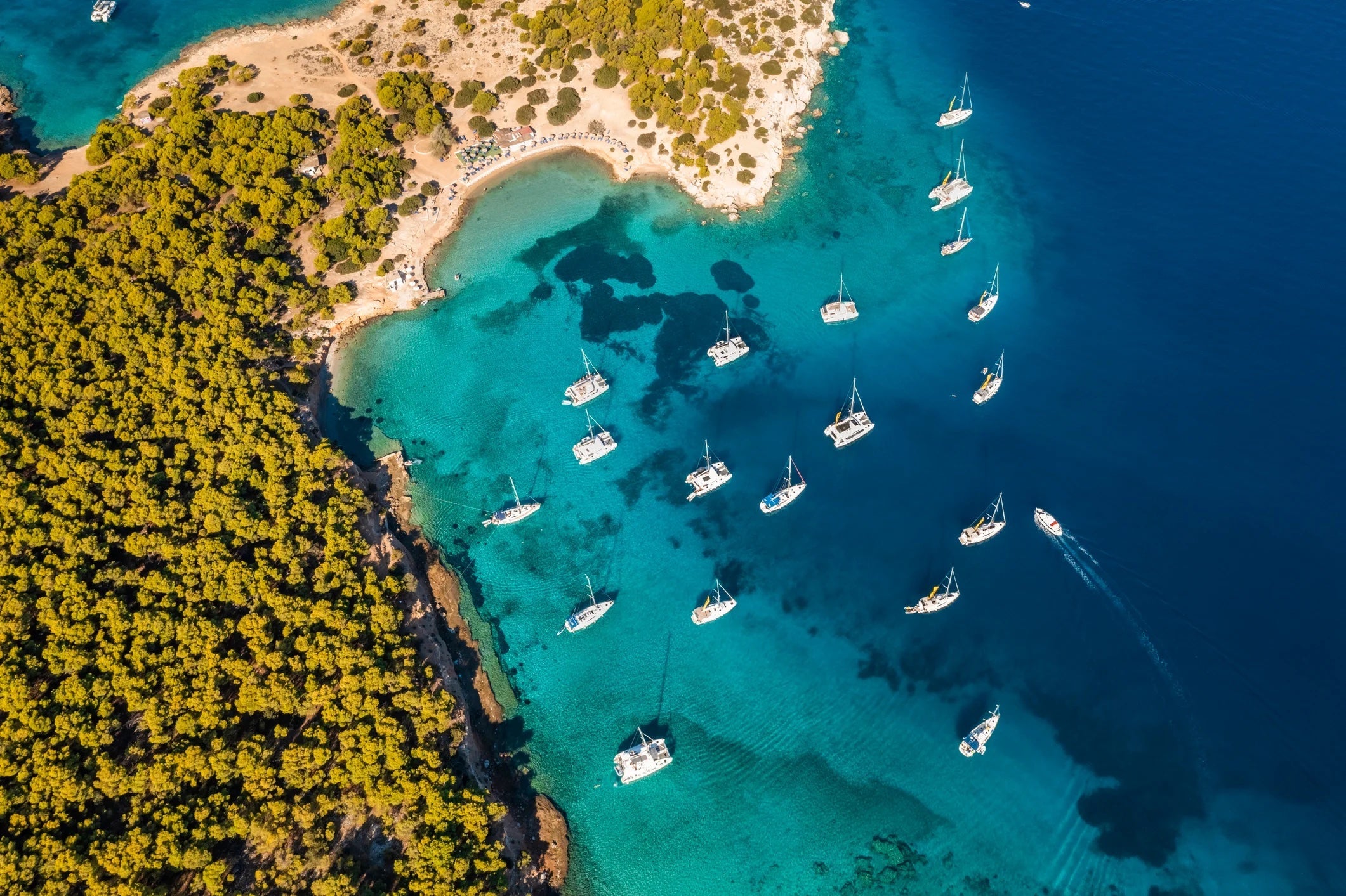 Yachts in turquoise water near the green island of Moni Eginas, Greece. Aerial view