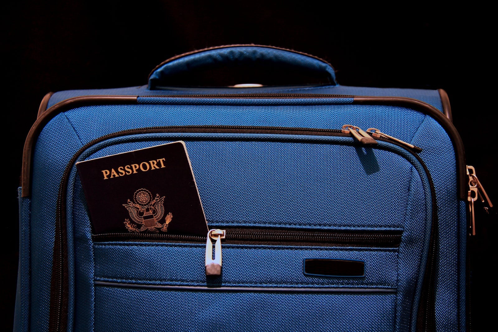 Blue suitcase and American passport on black background