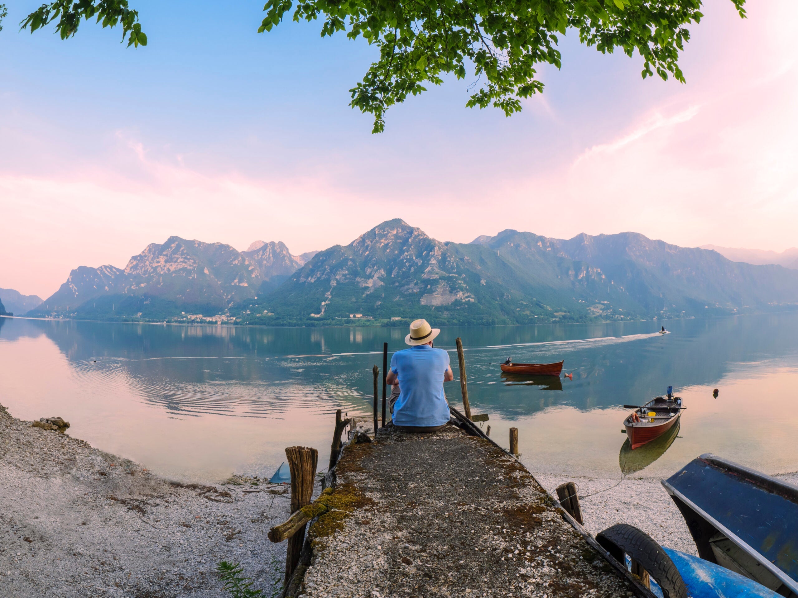 Italy, Lombardy, back view of man sitting on jetty at Lake Idro at morning twilight